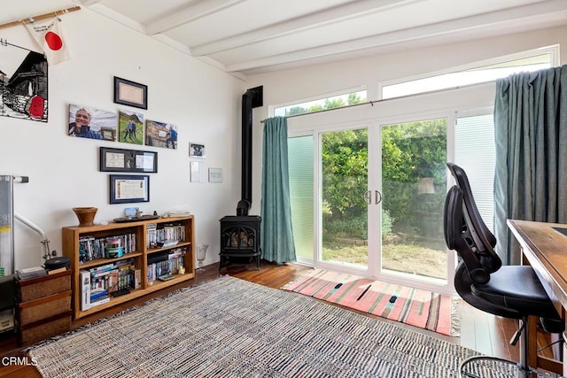 home office featuring beam ceiling, a wood stove, and wood finished floors