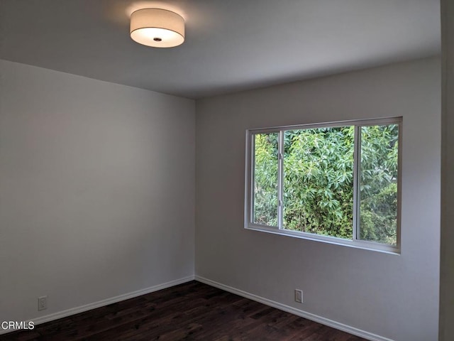 spare room with baseboards and dark wood-style flooring