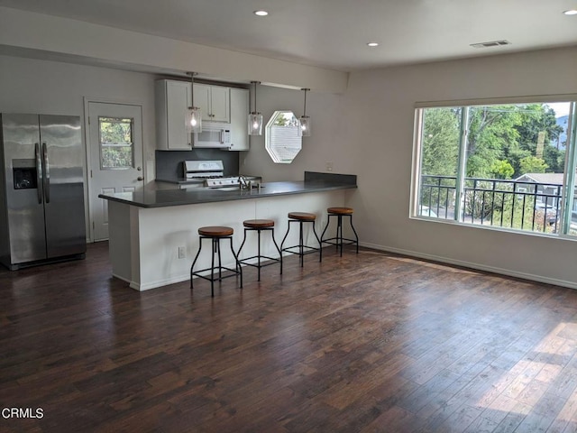 kitchen featuring visible vents, a kitchen bar, dark wood-style floors, white appliances, and a peninsula