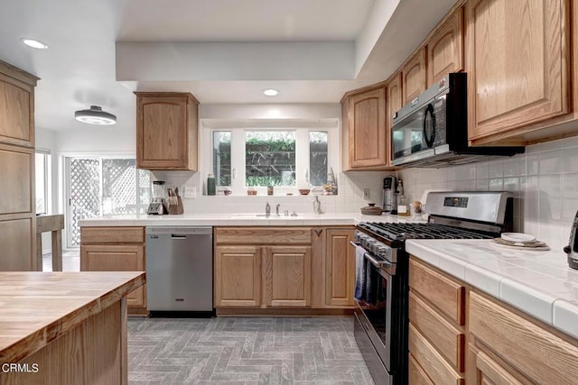 kitchen with a sink, backsplash, tile countertops, stainless steel appliances, and recessed lighting