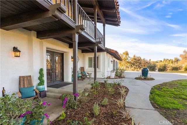 view of exterior entry featuring french doors, stucco siding, and a balcony