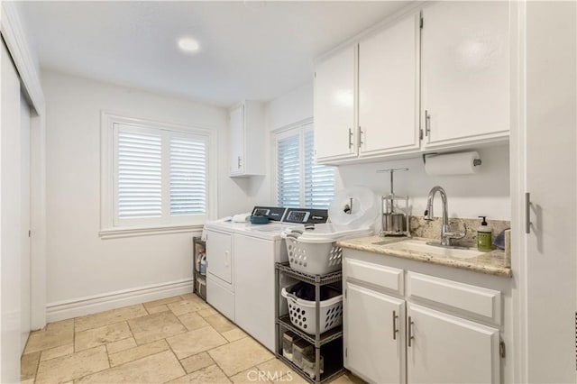 clothes washing area featuring a sink, cabinet space, stone tile flooring, washer and clothes dryer, and baseboards