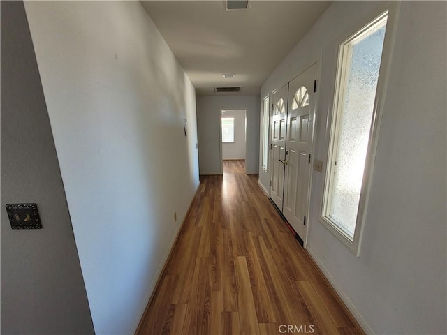 hallway with wood finished floors, visible vents, and baseboards