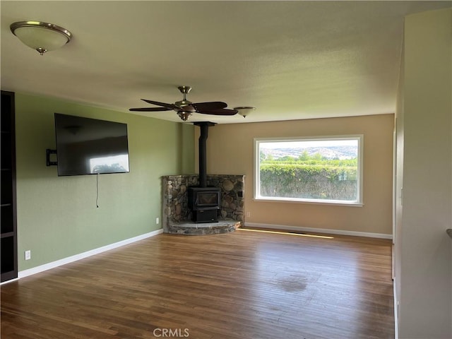 11122 Schafer Ave, Los Molinos, CA 96055 - unfurnished living room featuring a wood stove, wood finished floors, baseboards, and ceiling fan