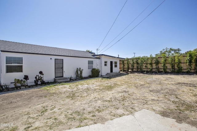 rear view of property with stucco siding, fence, and entry steps