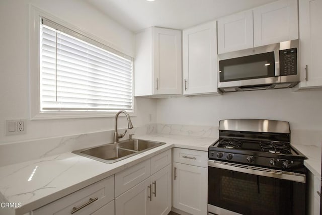 kitchen featuring light stone counters, appliances with stainless steel finishes, white cabinetry, and a sink