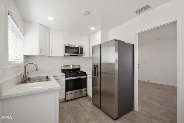 kitchen with visible vents, wood finish floors, a sink, stainless steel appliances, and white cabinetry