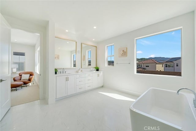 full bath with recessed lighting, double vanity, a freestanding tub, and a sink