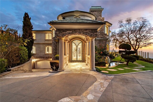 31821 Monarch Crst, Laguna Niguel, CA 92677 - exterior entry at dusk with stone siding, a chimney, and a lawn