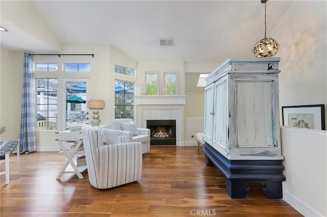 living room featuring a tiled fireplace, visible vents, baseboards, and wood finished floors