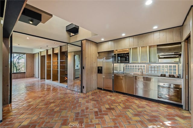 kitchen featuring recessed lighting, wooden walls, appliances with stainless steel finishes, and brick floor