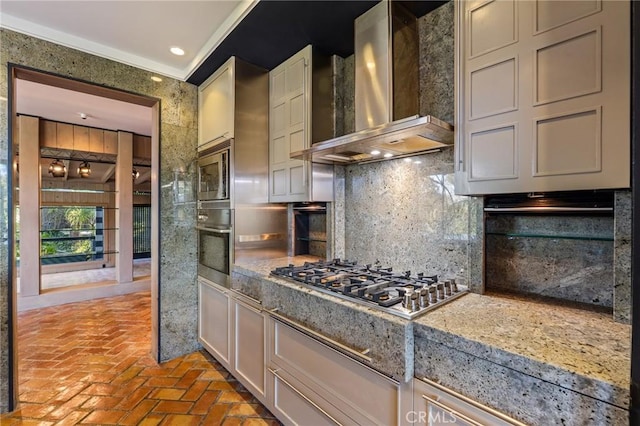 kitchen with wall chimney exhaust hood, brick floor, backsplash, and appliances with stainless steel finishes