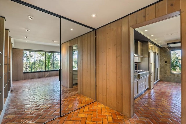 hallway featuring recessed lighting, brick floor, and wood walls