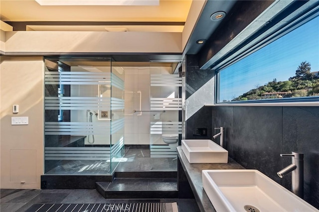 bathroom with a shower with shower door, toilet, and dual sinks