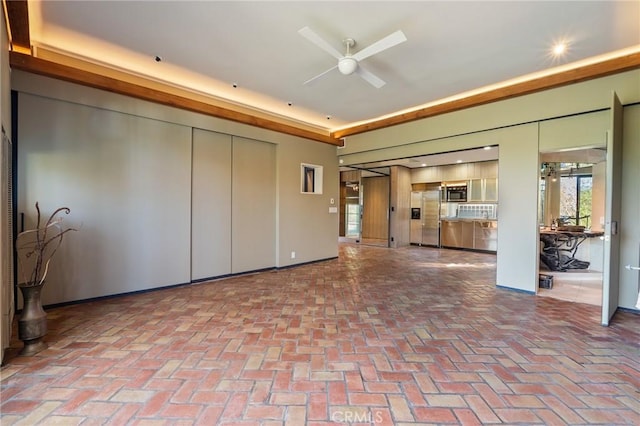 unfurnished living room featuring brick floor and a ceiling fan