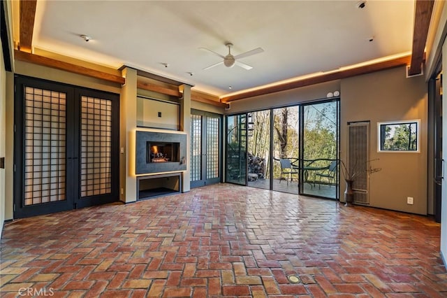 unfurnished living room featuring a ceiling fan, brick floor, and a healthy amount of sunlight
