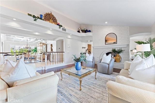 living area with wood finished floors, a brick fireplace, a chandelier, recessed lighting, and arched walkways