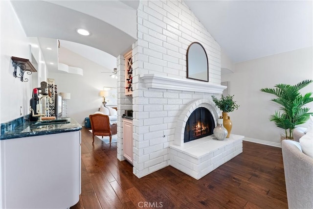 living area with vaulted ceiling, a brick fireplace, dark wood finished floors, ceiling fan, and recessed lighting