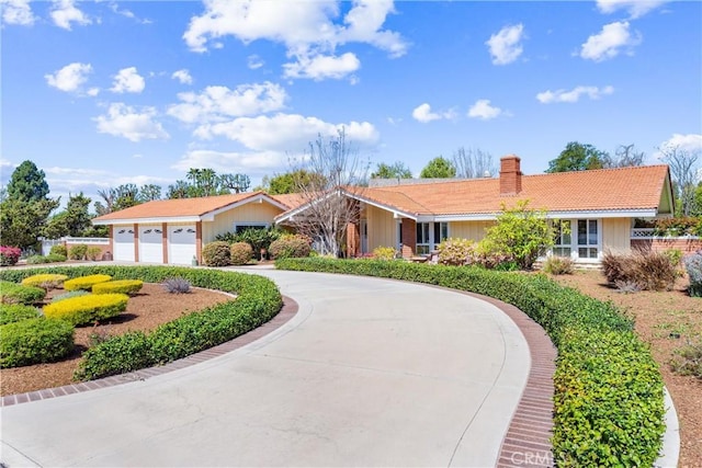 view of front of property with a chimney, a garage, curved driveway, and a tile roof