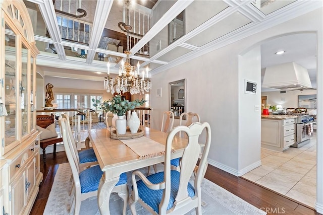 dining area with arched walkways, baseboards, light wood-type flooring, coffered ceiling, and ornamental molding