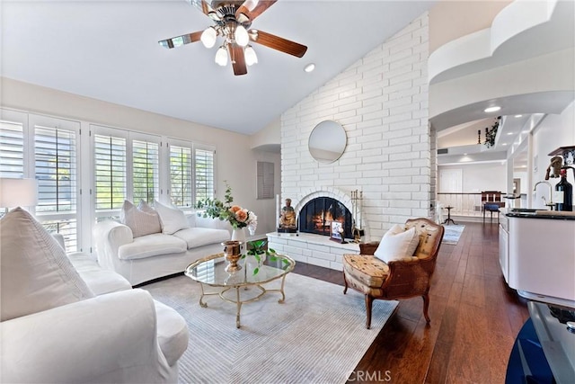 living room featuring a ceiling fan, high vaulted ceiling, dark wood-type flooring, a brick fireplace, and arched walkways