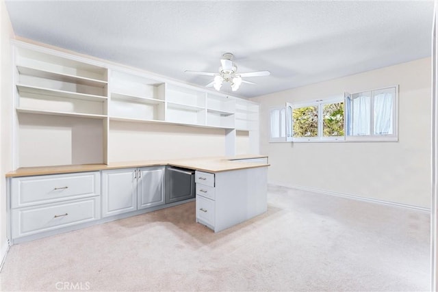 unfurnished office with light colored carpet, a ceiling fan, built in study area, baseboards, and a textured ceiling