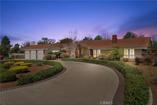 ranch-style house featuring a chimney, curved driveway, and a tile roof
