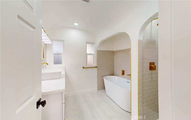 bathroom with a soaking tub, recessed lighting, vanity, and tile walls