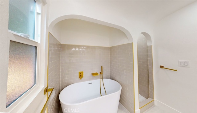 bathroom with a soaking tub and tile walls