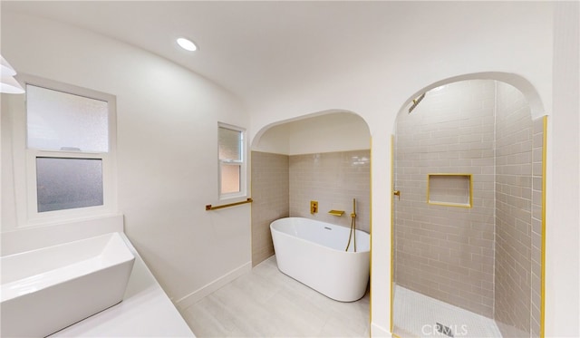 bathroom with recessed lighting, tiled shower, a freestanding tub, tile walls, and a sink