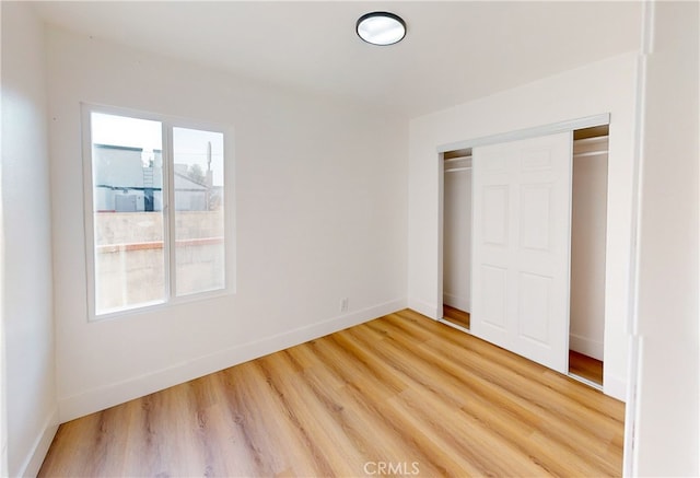 unfurnished bedroom featuring a closet, multiple windows, light wood-style floors, and baseboards