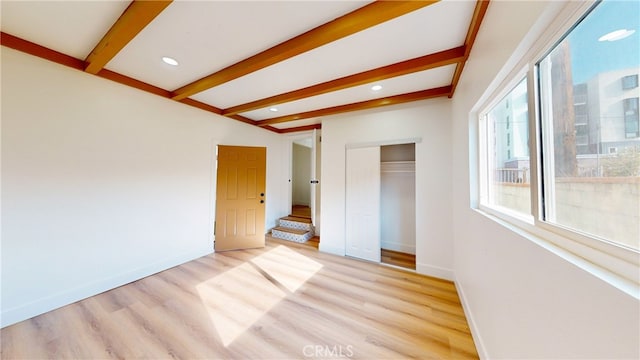 unfurnished bedroom featuring baseboards, beam ceiling, light wood-style floors, and a closet