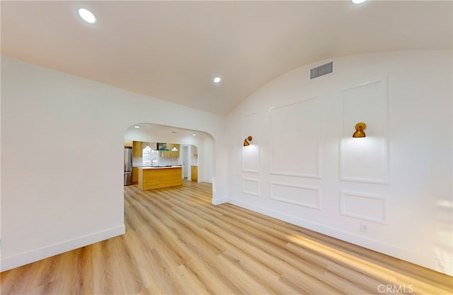 spare room featuring light wood finished floors, baseboards, lofted ceiling, recessed lighting, and arched walkways
