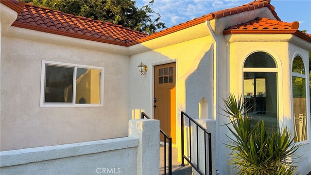 property entrance with stucco siding, a tiled roof, and fence