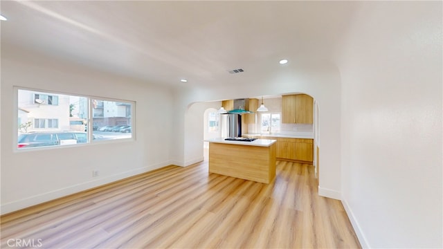 kitchen featuring visible vents, arched walkways, light countertops, light wood-style floors, and wall chimney exhaust hood