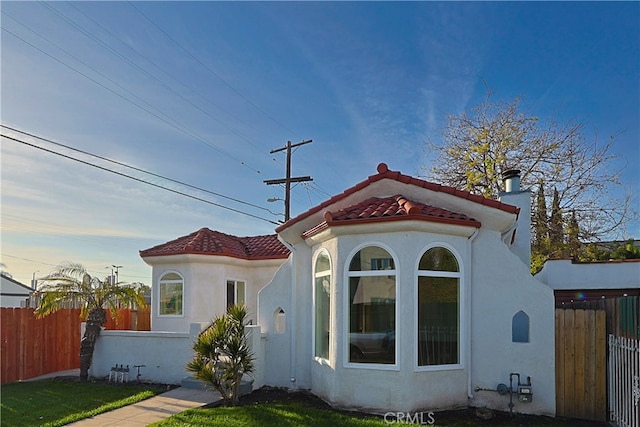rear view of property with stucco siding, fence, and a tiled roof