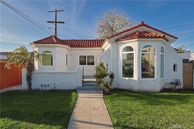 mediterranean / spanish-style house featuring a front yard, a tiled roof, fence, and stucco siding