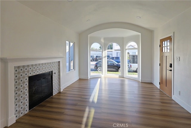 unfurnished living room with arched walkways, a fireplace, baseboards, and dark wood-style flooring