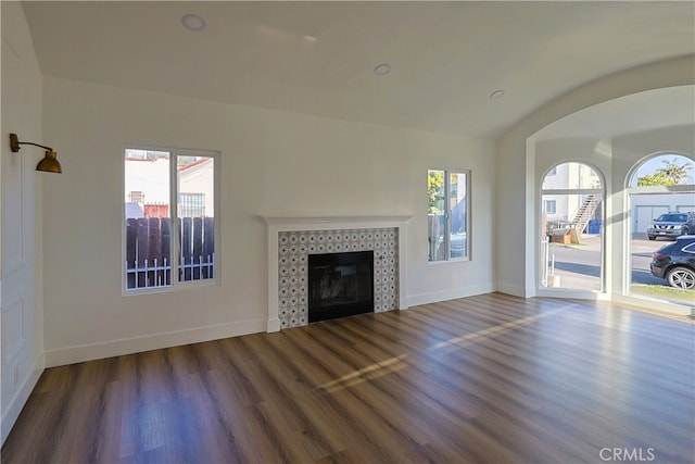 unfurnished living room with a tiled fireplace, plenty of natural light, baseboards, and wood finished floors