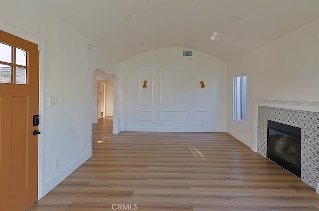 unfurnished living room with visible vents, baseboards, lofted ceiling, light wood-style flooring, and arched walkways