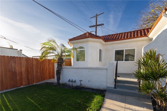 property entrance featuring stucco siding, fence, a lawn, and a tile roof