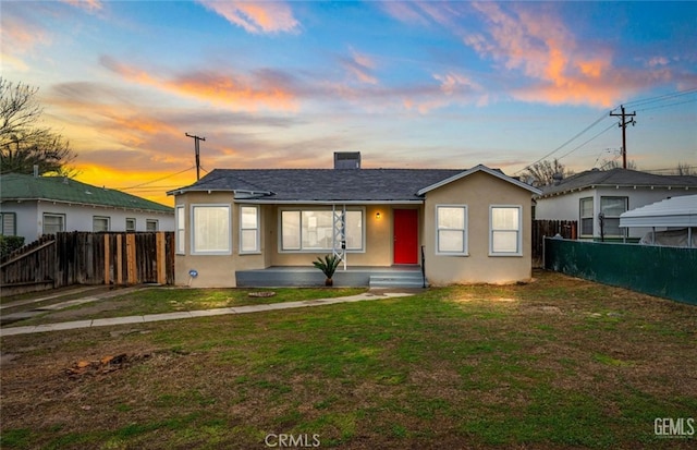 view of front of home featuring stucco siding, a lawn, and fence