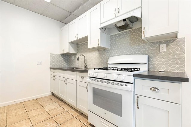 kitchen featuring dark countertops, backsplash, under cabinet range hood, white gas range, and a sink
