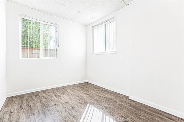 empty room with wood finished floors, baseboards, and a paneled ceiling