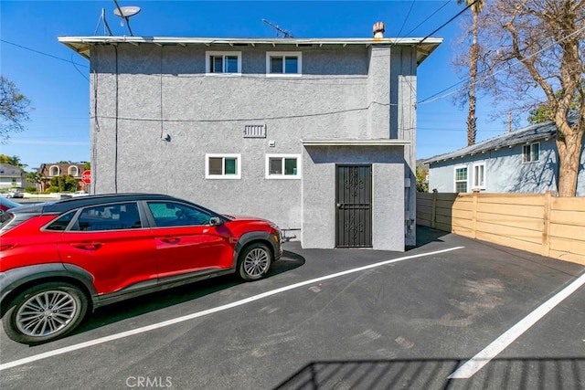 rear view of property featuring uncovered parking, fence, and stucco siding