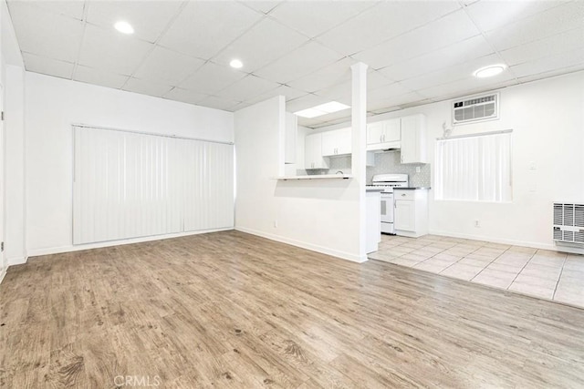 unfurnished living room with baseboards, a wall mounted air conditioner, a paneled ceiling, and light wood-style floors