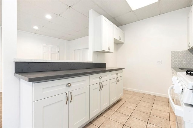 kitchen with stove, white cabinets, dark countertops, and a drop ceiling