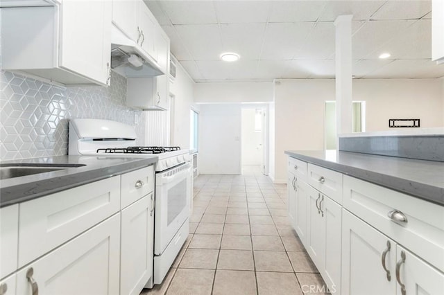 kitchen with light tile patterned floors, decorative backsplash, white cabinets, under cabinet range hood, and white gas range