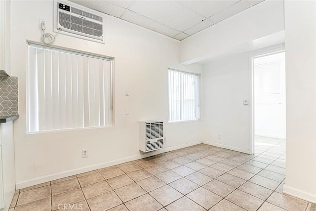 empty room featuring a wall mounted air conditioner, a paneled ceiling, heating unit, and light tile patterned floors