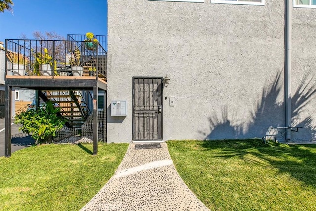 view of exterior entry with stucco siding, a yard, and a gate